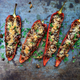 Five red romano pepper halves stuffed with filling lying face-up on a baking sheet